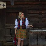 Fată îmbrăcată în port popular maramureșean tradițional, în fața unei case din lemn, la Popasul Izei – experiență autentică în Maramureș