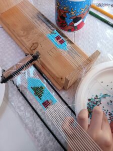 Atelier de confecționat zgărdane din mărgele la Popasul Izei, activitate tradițională pentru copii în Maramureș. Copii învață să confecționeze zgărdane din mărgele la războiul de țesut, activitate tradițională în tabără, Maramureș.
